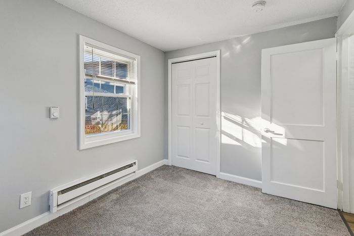Bright and inviting small room with plush carpet, sleek gray walls, and ample natural light through a charming window, perfect for a cozy retreat.