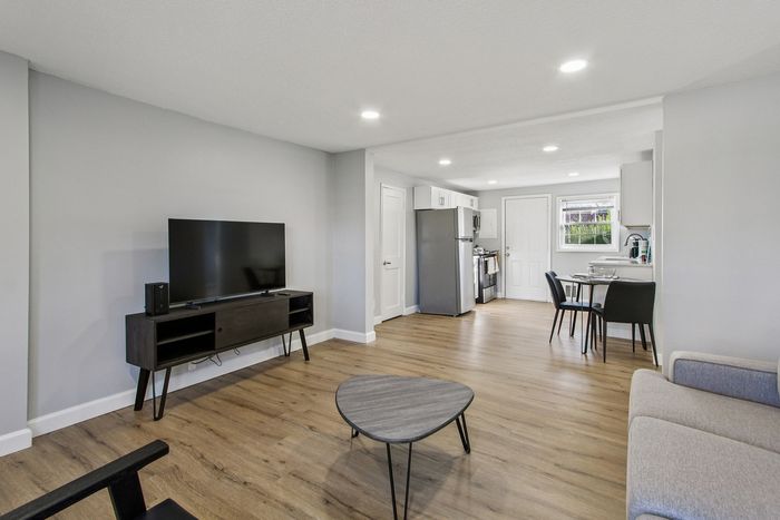Modern open-concept living area featuring sleek hardwood floors, stylish TV setup, and inviting dining space adjacent to a contemporary kitchen.