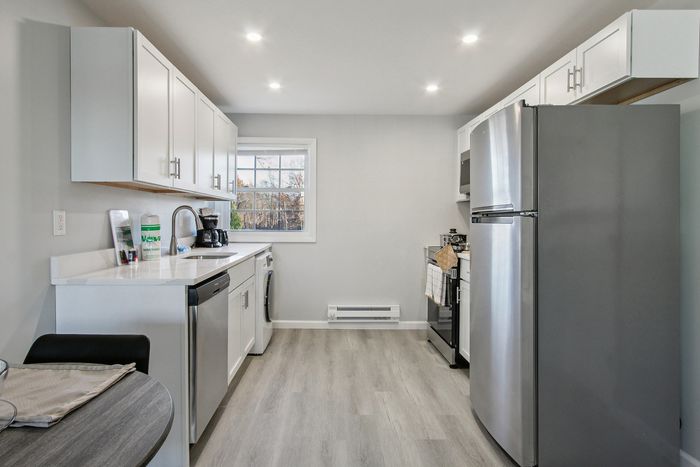 Modern kitchen with sleek stainless steel appliances, elegant white cabinets, and a bright window view. Ideal for culinary enthusiasts.