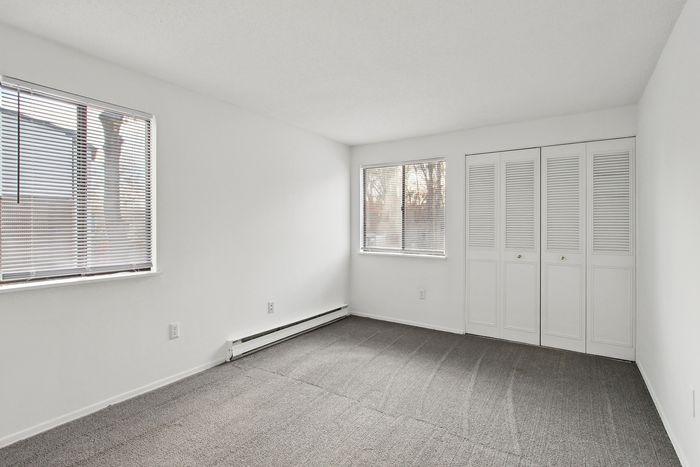 Bright and spacious bedroom with large windows and stylish closets, featuring fresh carpeting and abundant natural light.