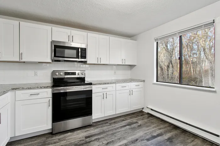 Bright modern kitchen with sleek white cabinets, stainless steel appliances, and a large window offering a serene forest view.