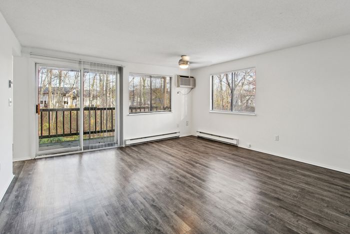 Bright living room with elegant hardwood floors, large windows, and a cozy balcony overlooking serene trees.
