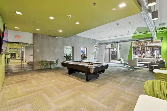Vibrant apartment amenity area with a pool table, modern seating, and green accents, ideal for leisure and social gatherings.