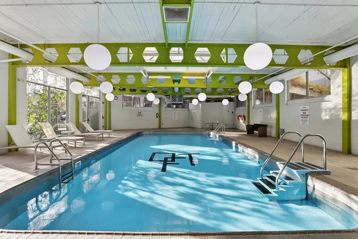 Bright indoor pool area with modern design, large windows, and relaxing lounge chairs.
