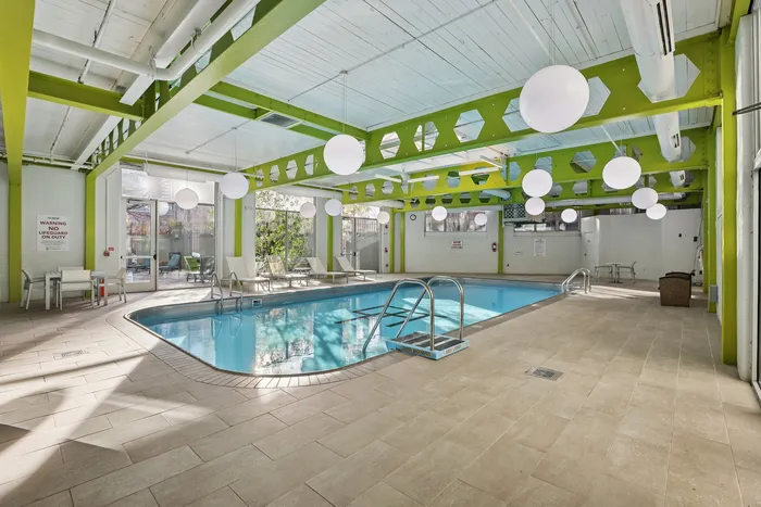 Vibrant indoor swimming pool area with modern green beams, ambient globe lighting, and comfortable sun loungers.