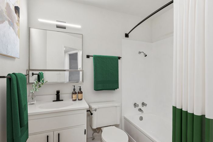 Contemporary bathroom with stylish green accents, featuring a sleek vanity, modern mirror, and a clean white bathtub with a matching shower curtain.