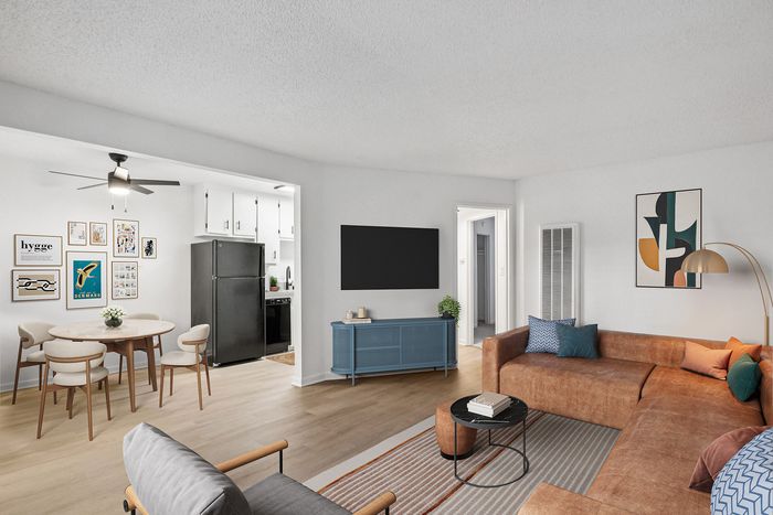 Modern living space with a cozy L-shaped sofa, vibrant wall art, open-plan kitchen and dining area, and sleek wooden floors.