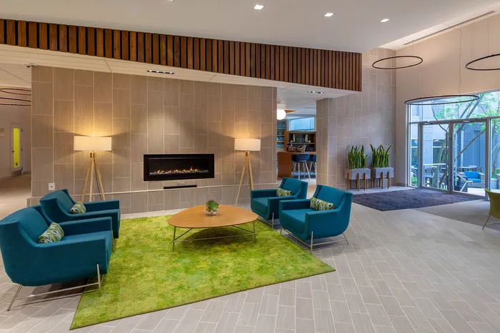 Chic modern lounge with cozy fireplace, vibrant blue chairs, and expansive windows offering plentiful natural light and courtyard views.