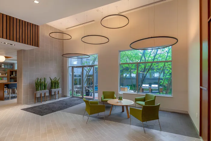 Modern lounge area with chic green chairs, elegant circular lighting fixtures, and large windows overlooking a serene outdoor space.