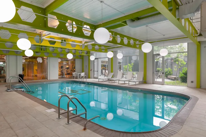 Modern indoor pool area with vibrant green accents, stylish lighting, and relaxational lounge chairs next to expansive windows.