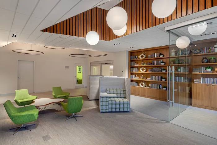 Modern lobby with elegant green seating, chic wooden accents, and a stylish glass-walled library area.