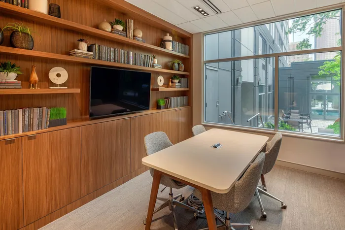 Modern apartment meeting room with sleek wooden shelves, stylish decor, and a large window offering a view of the cityscape.