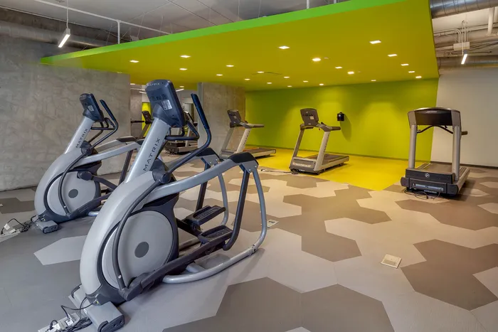 Modern fitness center featuring sleek exercise equipment, vibrant green accent wall, and geometric flooring.