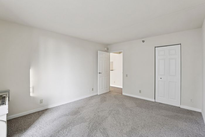 Bright and inviting room with plush carpet, fresh neutral walls, and ample natural light from a window, showcasing a spacious, serene ambiance.