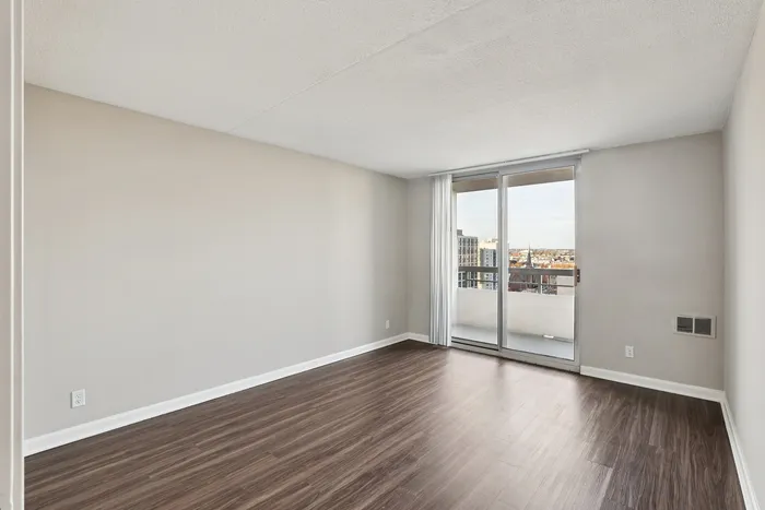 Bright, modern room with sleek wooden floors and large glass doors opening to a scenic balcony view.