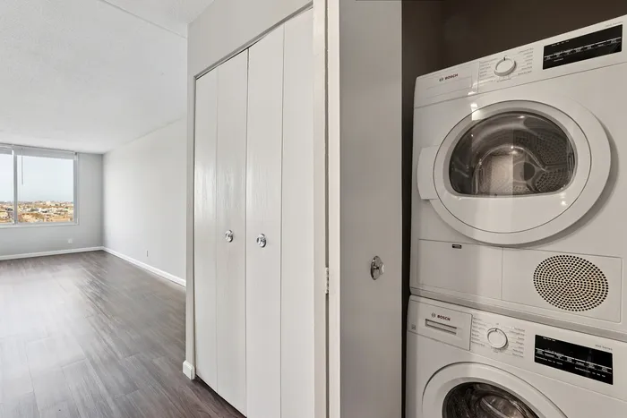 Modern apartment bedroom with sleek wood flooring, large window with city views, and in-unit Bosch washer and dryer.