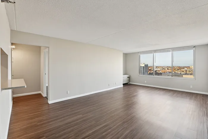 Expansive living area with sleek wooden flooring, large windows offering stunning city views, and a modern architectural design perfect for stylish urban living.