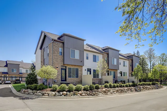 Charming row of modern townhouses with stylish brickwork, large windows, and lush landscaping on a sunny day.