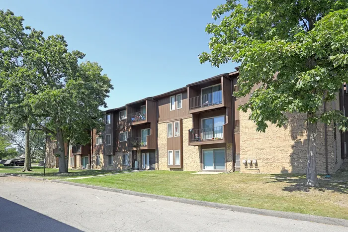 Charming three-story apartment building with private balconies, nestled among lush trees and manicured green lawns.