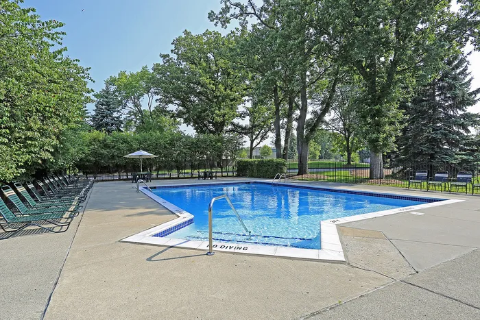 Inviting outdoor pool area surrounded by lush trees and ample seating, perfect for relaxation and enjoyment.