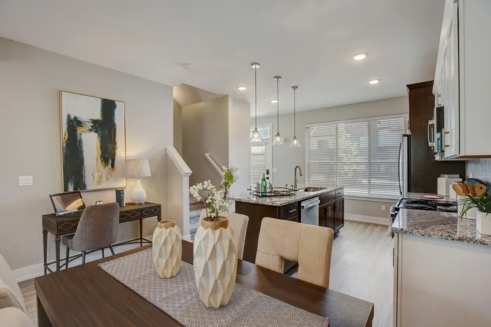Modern open-concept dining and kitchen area with stylish décor, natural light, and a chic island with pendant lighting.