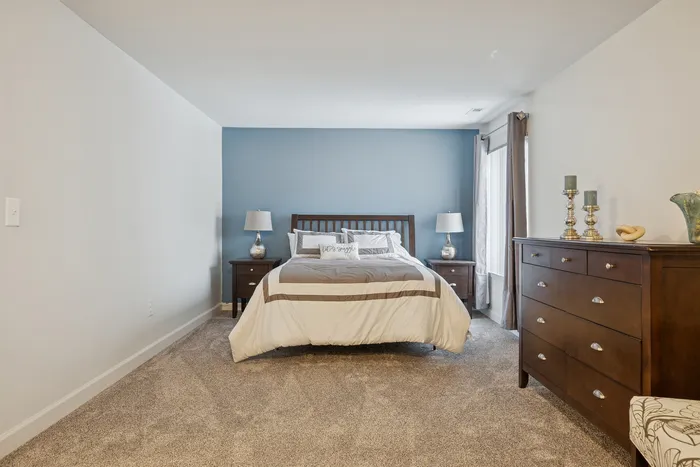 Inviting bedroom with plush carpet, elegant blue accent wall, and sophisticated dark wood furniture including a cozy bed flanked by stylish lamps.