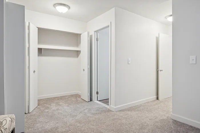 Modern apartment interior showcasing a spacious open closet with double doors, adjacent to crisp white walls and plush carpet flooring.