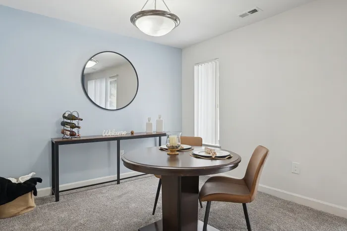 Elegant dining area with cozy round table, stylish chairs, and welcoming decor featuring a mirror and table with wine rack.