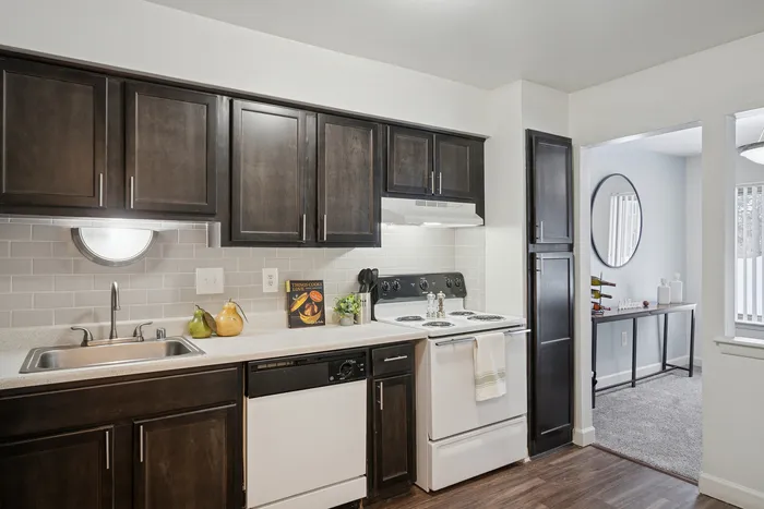 Modern kitchen with dark wood cabinets, sleek countertops, and stainless steel appliances, seamlessly opening into a cozy living area.