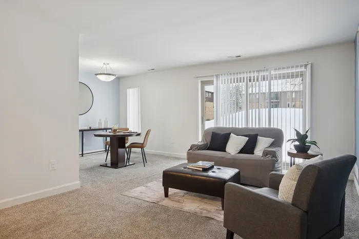 Inviting living space featuring modern gray sofa, chic dining area, and large windows with vertical blinds allowing for abundant natural light.