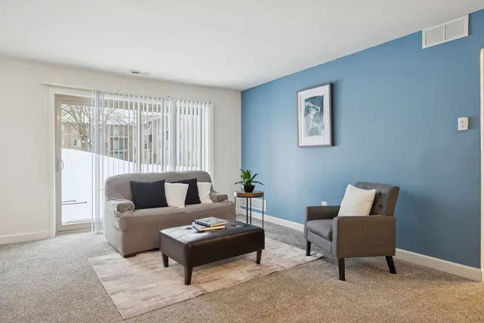 Bright and inviting living room with modern gray furniture, blue accent wall, and natural light streaming through large windows.