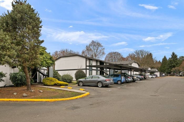 Inviting apartment community with covered parking, lush greenery, and peaceful surroundings under a clear blue sky.
