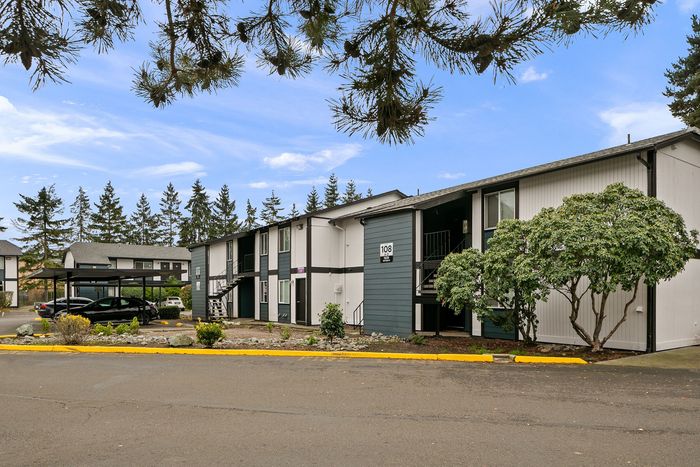 Charming apartment complex nestled among lush trees, featuring modern architecture and convenient parking.