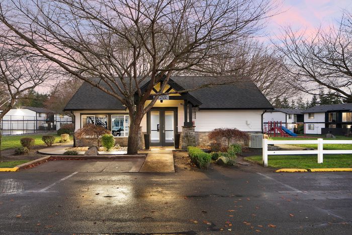 Charming community center with modern architecture, surrounded by lush greenery and a nearby playground, under a picturesque evening sky.