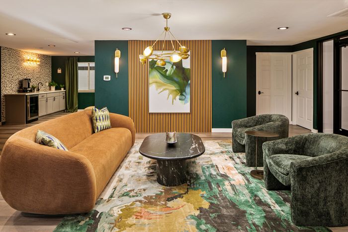 Chic living room with a modern mustard sofa, elegant dark green chairs, and a stylish art piece on an accent wall. Features a sleek black coffee table on a vibrant patterned rug.