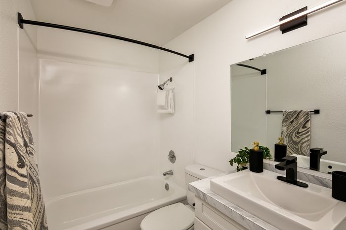 Modern bathroom featuring a sleek white bathtub, elegant vanity with marble countertop, and stylish black fixtures.