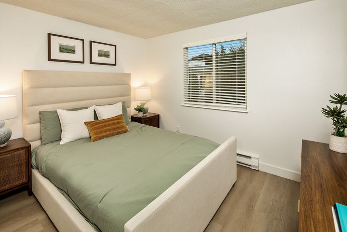 Charming bedroom featuring a plush beige bed with green accents, soft lighting, and modern wood flooring for a cozy retreat.