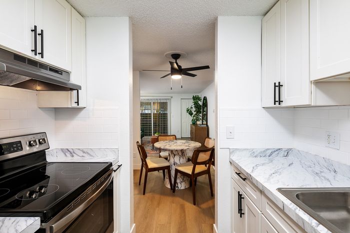 Inviting kitchen with modern white cabinets, elegant marble countertops, and a view into a cozy dining area featuring a chic round table and stylish chairs.