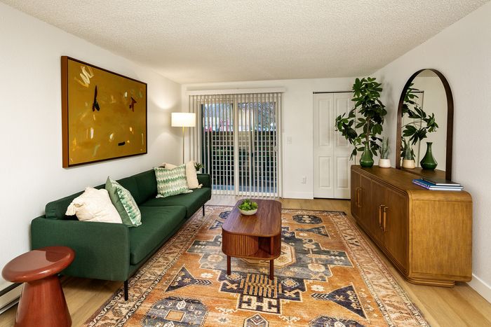 Chic living room with an elegant green sofa, artistic wall decor, and a warm wooden console. Stylish rug and vibrant plants create a cozy ambiance.