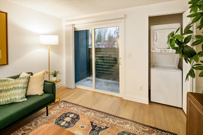 Cozy living space with a stylish green sofa, natural light-filled sliding glass door, and in-unit laundry for modern convenience.