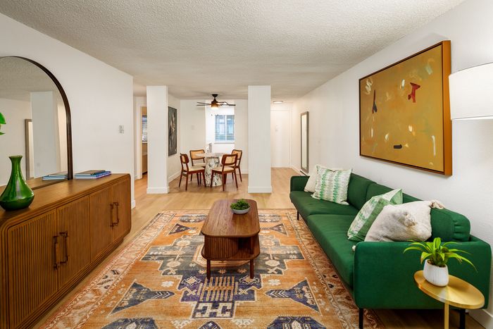 Inviting open-concept living and dining area with a stylish green sofa, artistic rug, and elegant wooden decor, ideal for modern living.