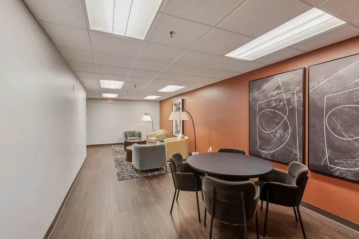 Modern lounge area featuring stylish seating with plush armchairs, contemporary round table, and captivating abstract art on a warm-toned accent wall.