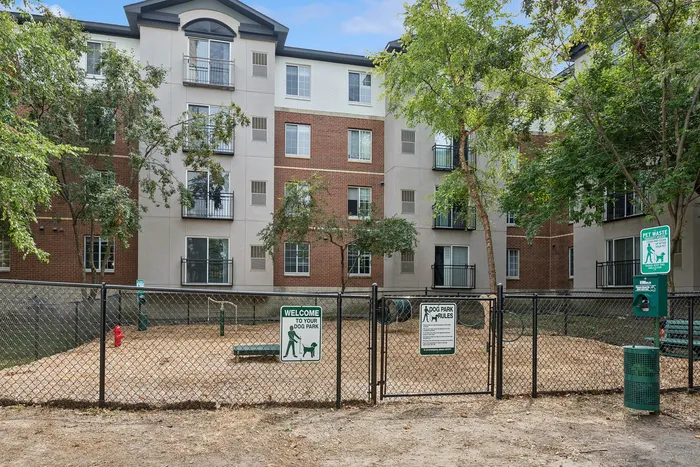 Inviting community dog park nestled within a modern apartment complex, featuring lush trees and ample open space.