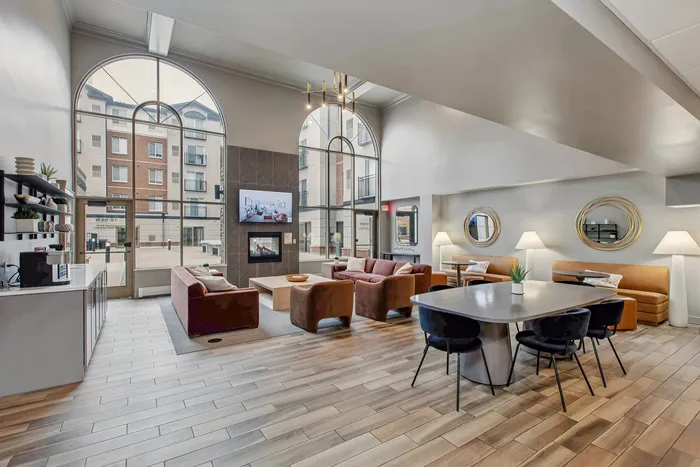 Elegant apartment lounge with high ceilings, modern furniture, large arched windows, and a cozy fireplace.