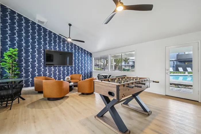 Chic contemporary lounge with stylish seating, modern foosball table, and a view of a refreshing pool area.