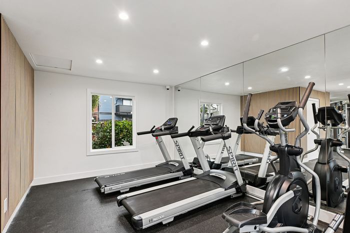 Modern apartment fitness room with treadmills and exercise equipment, featuring mirrored walls and natural light.