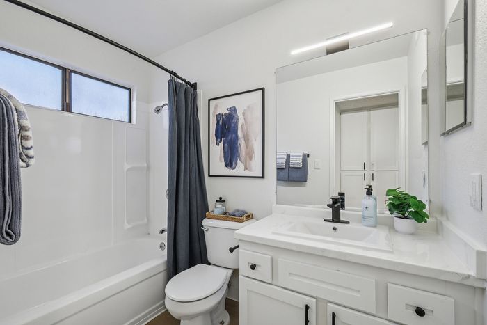 Bright and modern bathroom featuring elegant white cabinetry, a stylish black faucet, and a serene artwork on the wall. Includes a sleek mirror, fresh potted plant, and plush towels, creating a sophisticated, spa-like ambiance.