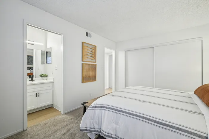 Bright and elegant bedroom with cozy white bedding, modern artwork on the wall, and an ensuite bathroom with sleek fixtures.