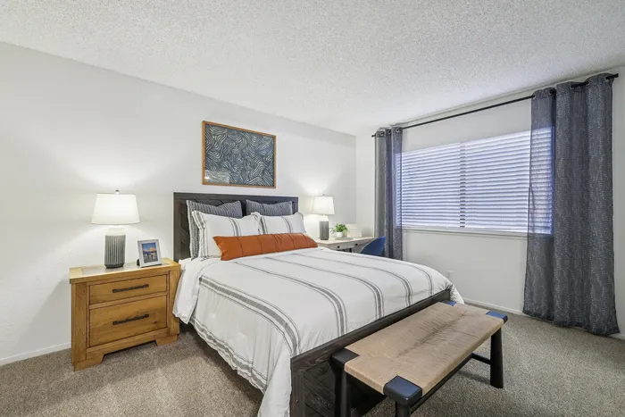 Bright and inviting bedroom with modern decor, featuring a cozy bed with striped linens, stylish wooden nightstand, and large window with elegant curtains.