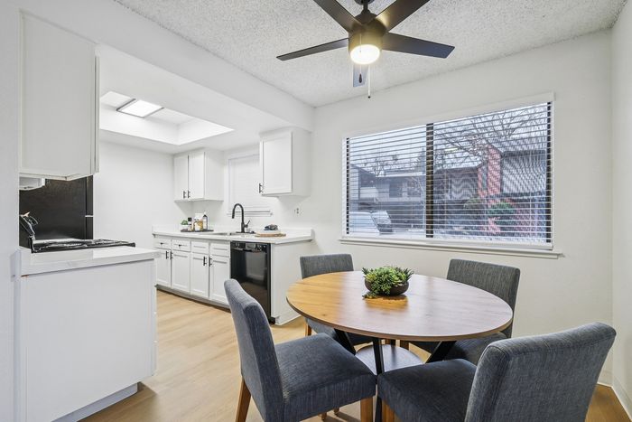 Charming open kitchen with sleek white cabinetry, modern appliances, and a cozy dining area with stylish chairs, bathed in natural light from large windows.